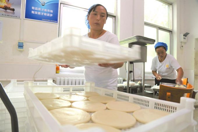 在潼关县潼蘇祥肉夹馍生产加工基地，工人们正在把成型的肉夹馍饼盛放在馍筐中，这些面饼将被送往塑封包装车间。 本版图片均由本报记者 郑栋摄